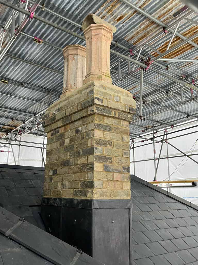 Stone chimney under scaffolding with two chimney pots