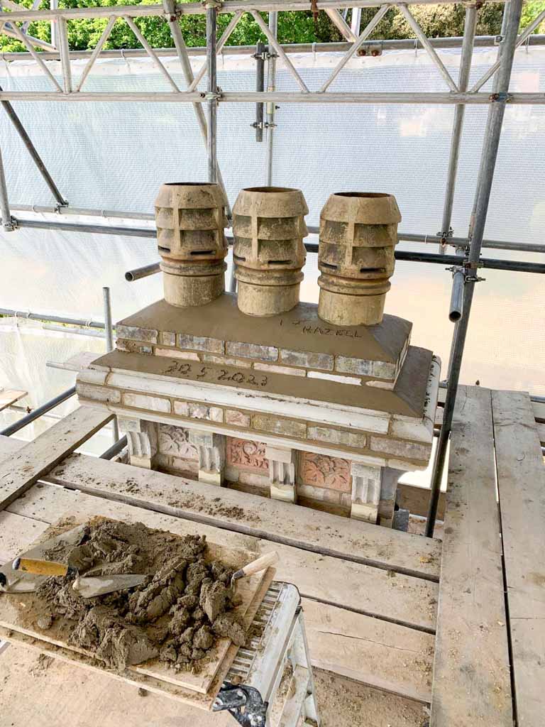Ornate stone chimney with three chimney pots under scaffolding